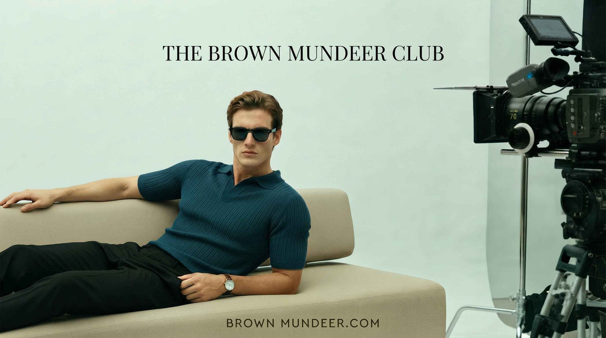 Man in a blue short-sleeve knit polo and sunglasses lounging on a beige sofa.